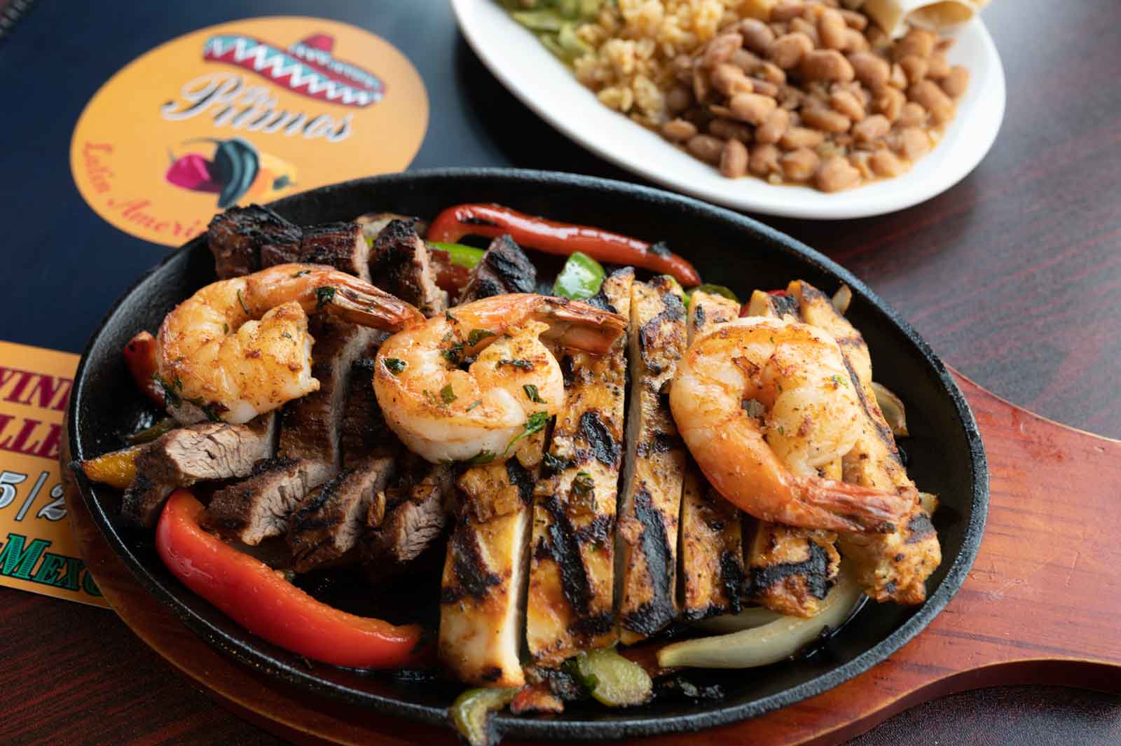 Mixed fajitas with steak, chicken and shrimp on a hot skillet next to rice and beans